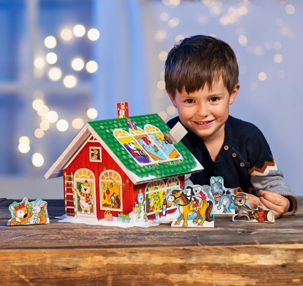 Malý chlapec stavící adventní domeček ze dřeva a papíru